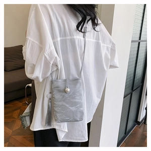 Détail du sac plissé gris avec fermoir perle et pompon porté sur une chemise blanche