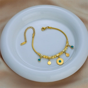 Gold stainless steel beaded bracelet with turquoise pendant on white ceramic plate