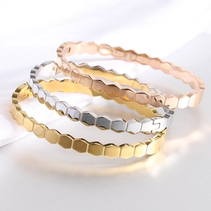 Close-up of three hexagonal honeycomb bangles in gold, silver, and rose gold finishes