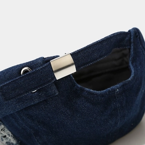 Detail of adjustable metal buckle and distressed denim fabric on back of the docker cap