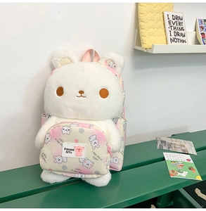Detailed close-up of white plush bunny backpack with pink printed front pocket on a bench