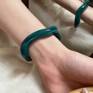 Detail of dark green resin bangle with marble texture on soft pleated fabric