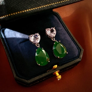 Detailed view of silver heart and pear-cut green zircon earrings on velvet display