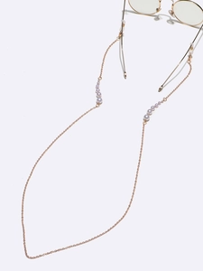 Golden eyewear chain with high-luster pearls attached to round glasses on grey background