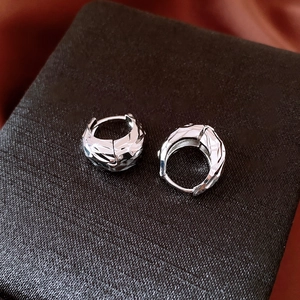 Macro shot of silver U-shaped hoop earrings with pleated striped texture on silk fabric
