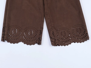 Detail of dark brown faux suede pants featuring intricate laser-cut hollow floral patterns