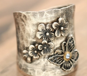 Detail of vintage textured silver ring featuring embossed floral patterns and blue rhinestone butterfly
