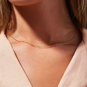 Detailed close-up of a minimalist gold beaded chain necklace on a model's neck