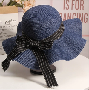 Detail of navy blue woven sun hat featuring a striped bow and large wavy brim for beach