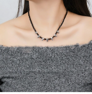 Close-up of black beaded necklace with silver skull charms worn by a model in soft lighting