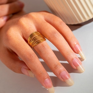 Detail of a gold multilayer coil ring on a model hand with warm lighting and a soft vibe