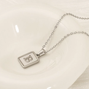 Macro shot of a rectangular silver-tone necklace with a letter B pendant on a ceramic dish