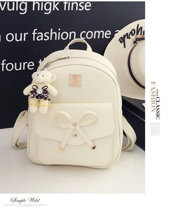 Detailed view of creamy white bow backpack with gold logo and plush bear charm
