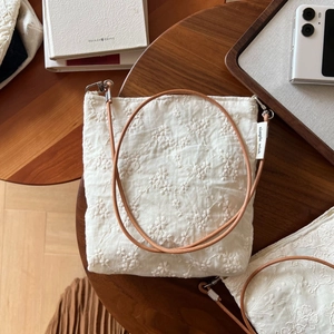 Close-up of small floral embroidery on beige linen bag with slim brown leather strap