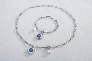 Detail of silver paperclip chain necklace and bracelet set with blue gems and pearls