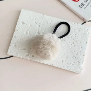 Detailed close-up of a soft grey plush pom pom hair tie on a white stone display block