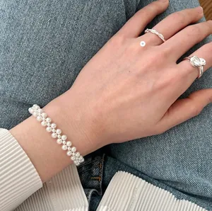 Close-up of knotted silver rings and double-layer pearl bracelet on hand