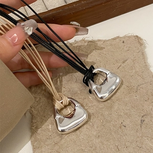Dettaglio di ciondoli a borsa geometrici su cordoncini intrecciati neri e beige