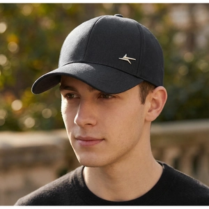 Detail of black cotton baseball cap with silver metal logo worn by a male model outdoors