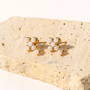 Macro detail of cross shaped stud earrings with white pearls and gold metal base