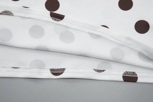 Gros plan sur les doubles coutures de l'ourlet à pois marron sur le tissu blanc