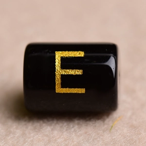 Macro shot of black cylindrical bead with gold stamped letter E for DIY jewelry