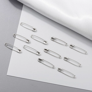 Flat lay macro of ten polished silver steel safety pins on silk and grey paper background