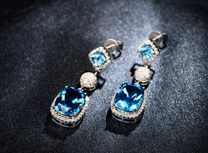 Macro shot of long drop earrings featuring large rectangular aquamarine gems and diamonds