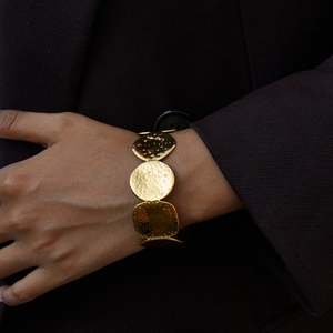 Detailed view of wide golden hammered metal cuff featuring geometric linked shapes