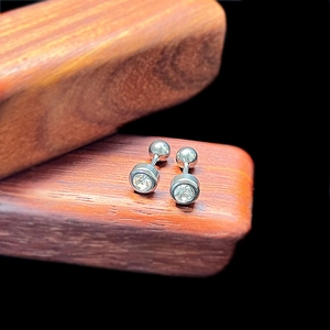Macro shot of silver screw-back stud earrings with round zircons on a wooden base