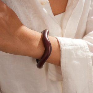 Detail shot of a dark reddish-brown irregular acrylic bangle on a white linen shirt sleeve
