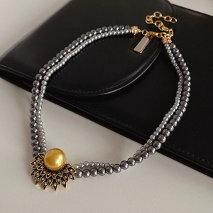 Detail of vintage double-layer grey pearl necklace with a golden sunburst pendant