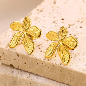 Detail of golden flower earring showing brushed texture and petals on beige stone