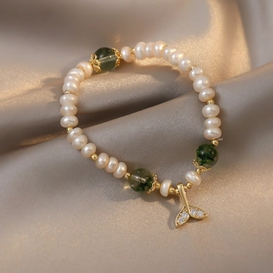 Detailed close-up of Baroque freshwater pearl bracelet with green beads and gold fish tail charm