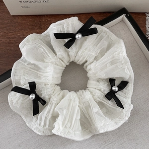 Detailed shot of white lace scrunchie with black bows and imitation pearls on mesh fabric