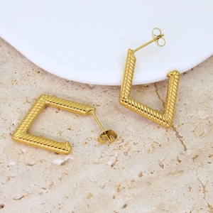 Close-up of golden geometric square earrings with a twisted texture on marble base