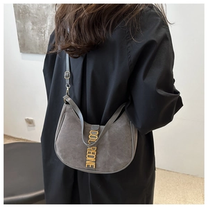 Detail of grey suede shoulder bag with metallic logo bar on a model with black outfit