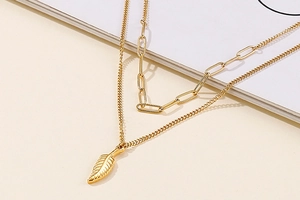 Detailed close-up of double-layered gold wing necklace with chunky chain and feather pendant