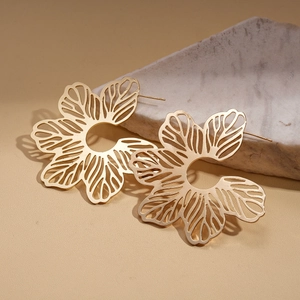Macro detail of golden hollow flower stud earrings with a refined matte metal finish