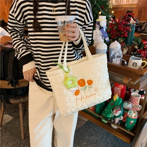 Quilted white canvas tote bag with tulip embroidery and flower charm in use