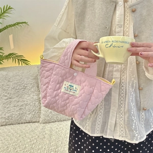 Close-up of pink quilted heart bag featuring a Happy embroidered patch and top handle