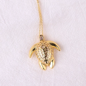 Detail of a gold turtle necklace pendant inlaid with sparkling baguette-cut clear stones