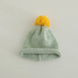 Close-up of knit texture on blue-green kids beanie with a bright yellow pom-pom