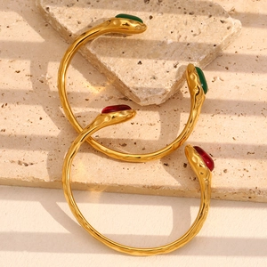 Close-up of gold snake head bangles with red and green stones on travertine background