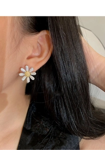 Detail of sparkling white and yellow zircon daisy stud earrings worn on the ear