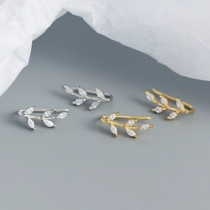 Detailed view of silver and gold leaf-shaped ear cuffs with marquise crystals on grey background