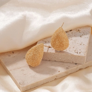 Elegant gold teardrop earrings with a grainy metal texture on a neutral stone background