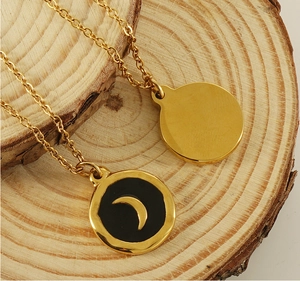 Detail of gold moon pendant with black enamel inlay on natural wood background