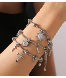 Detail of layered stainless steel bracelets with heart, cross, and sun charms on wrist