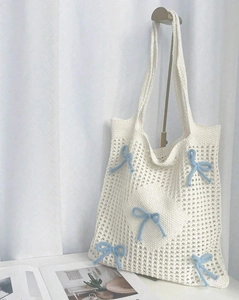 Detail of white hollow crochet tote bag featuring light blue ribbon bows and cotton texture